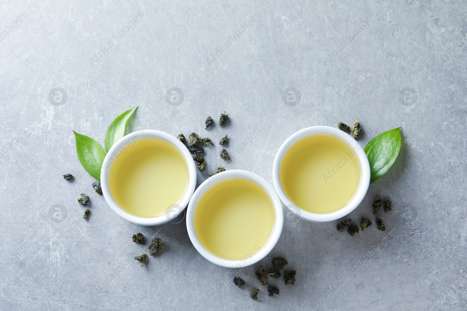 Photo of Cups of Tie Guan Yin oolong and tea leaves on grey background, top view with space for text