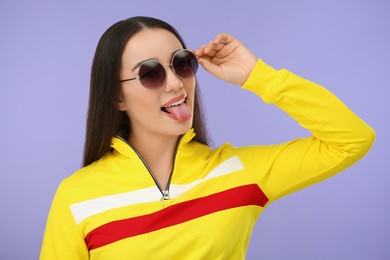Photo of Happy woman in sunglasses showing her tongue on violet background