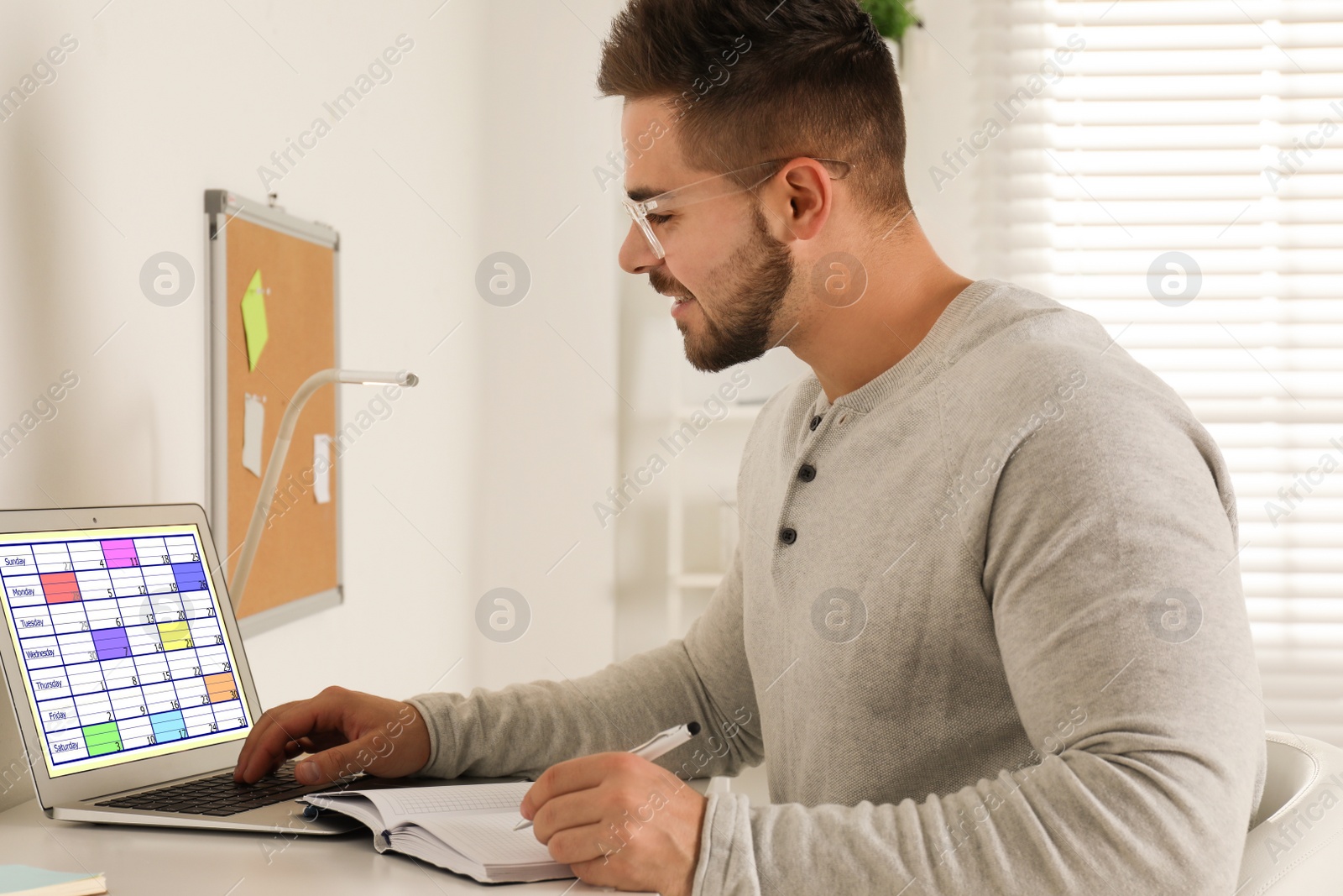 Photo of Young man using calendar app on laptop in office