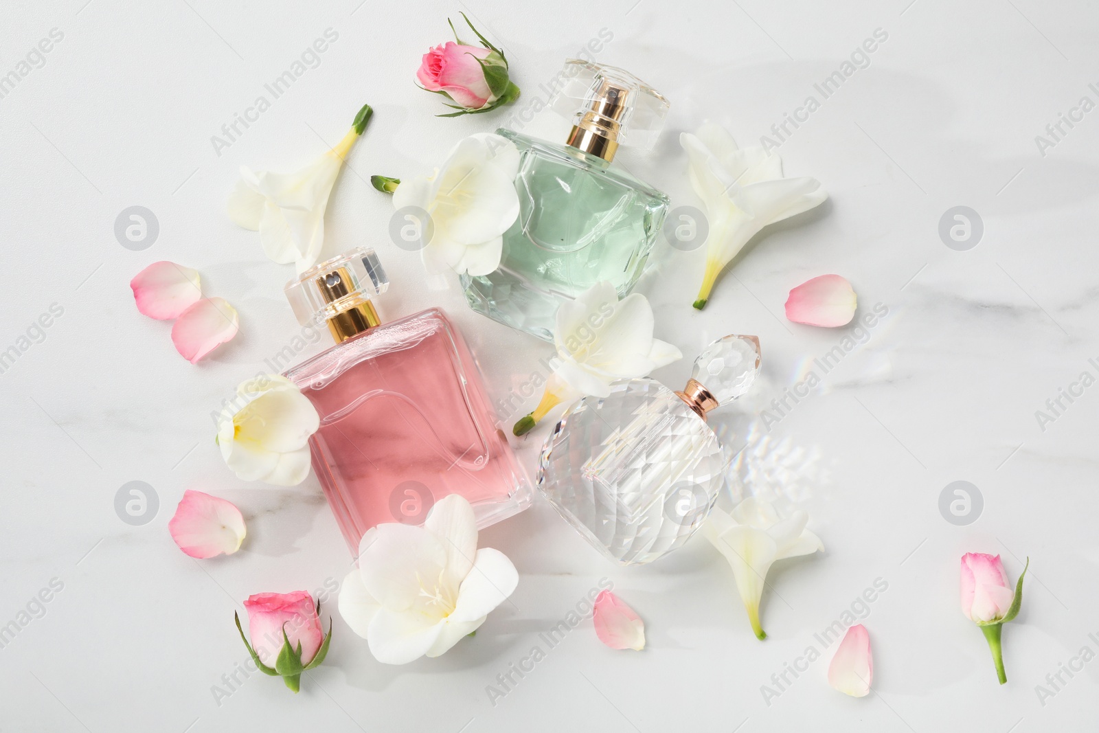 Photo of Luxury perfume and floral decor on white marble table, flat lay