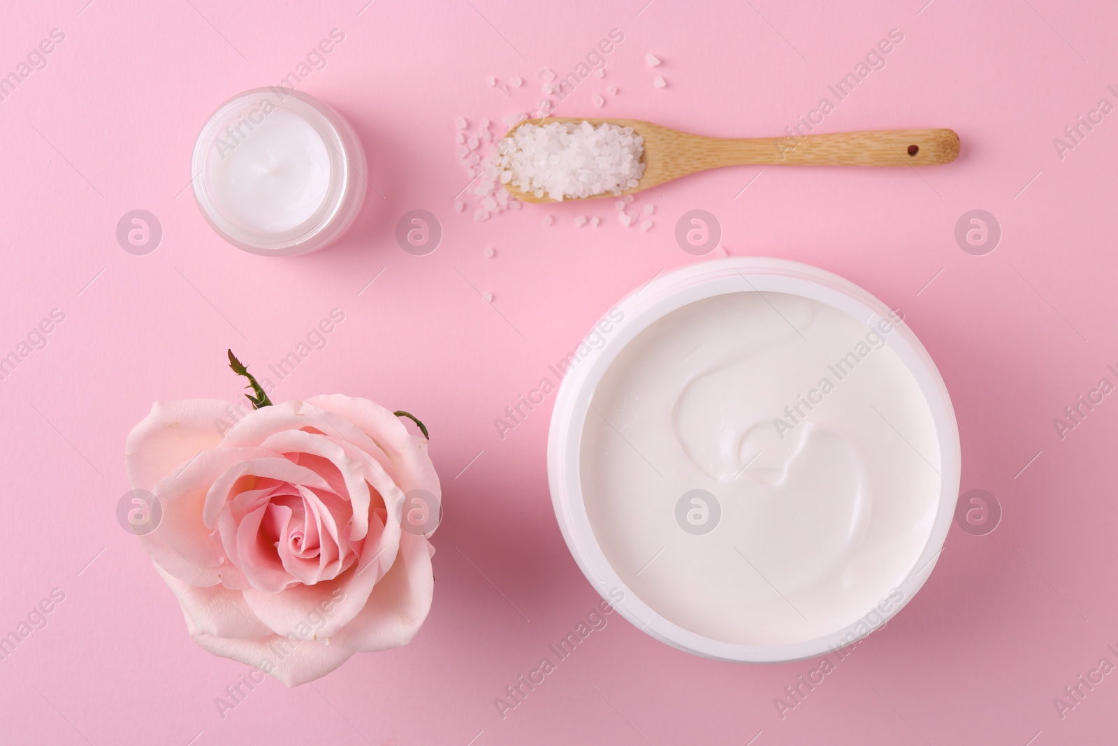 Photo of Jars of cream, sea salt and rose flower on pink background, flat lay. Body care products