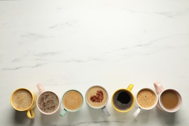 Many cups with different aromatic coffee drinks on white marble table, flat lay. Space for text