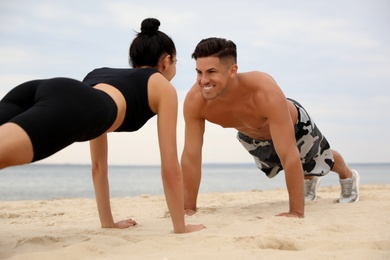 Photo of Couple doing exercise together on beach. Body training