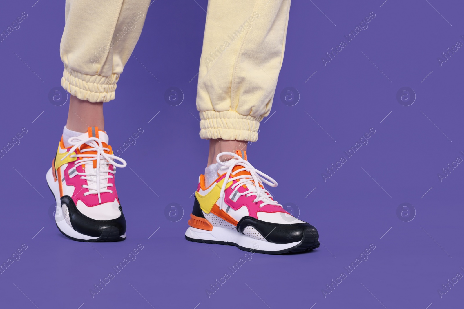 Photo of Woman wearing pair of new stylish sneakers on purple background, closeup