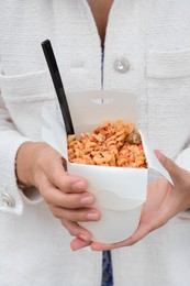 Photo of Woman holding paper box of takeaway noodles with fork, closeup. Street food