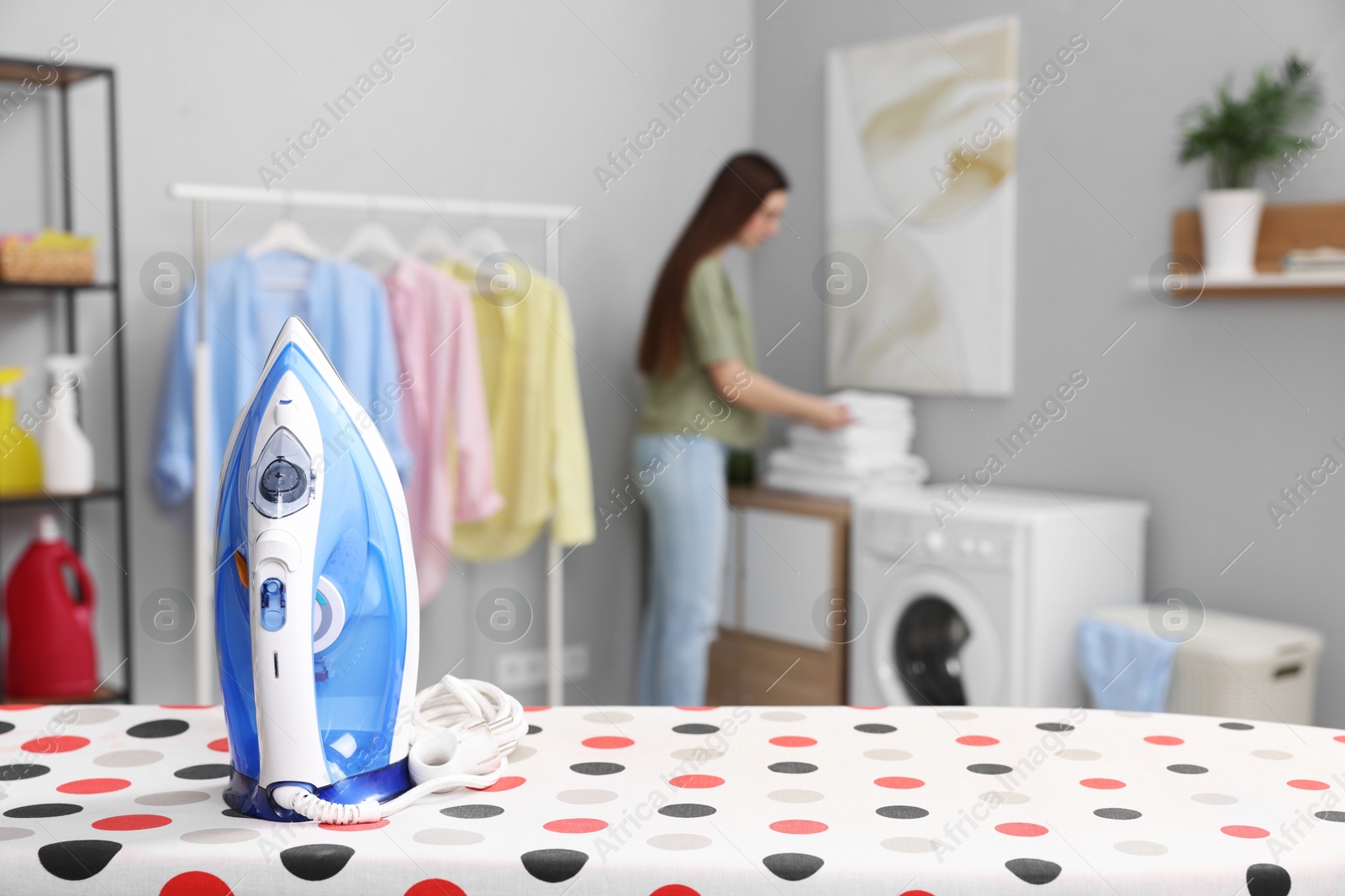 Photo of Woman with towels in laundry room, focus on clothes iron