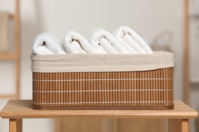 Photo of Wicker basket with folded soft terry towels on wooden table indoors