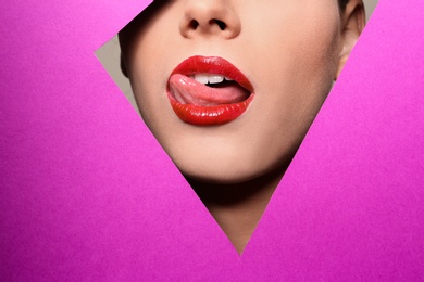 Photo of View of beautiful young woman with red lips through cutout in color paper, closeup