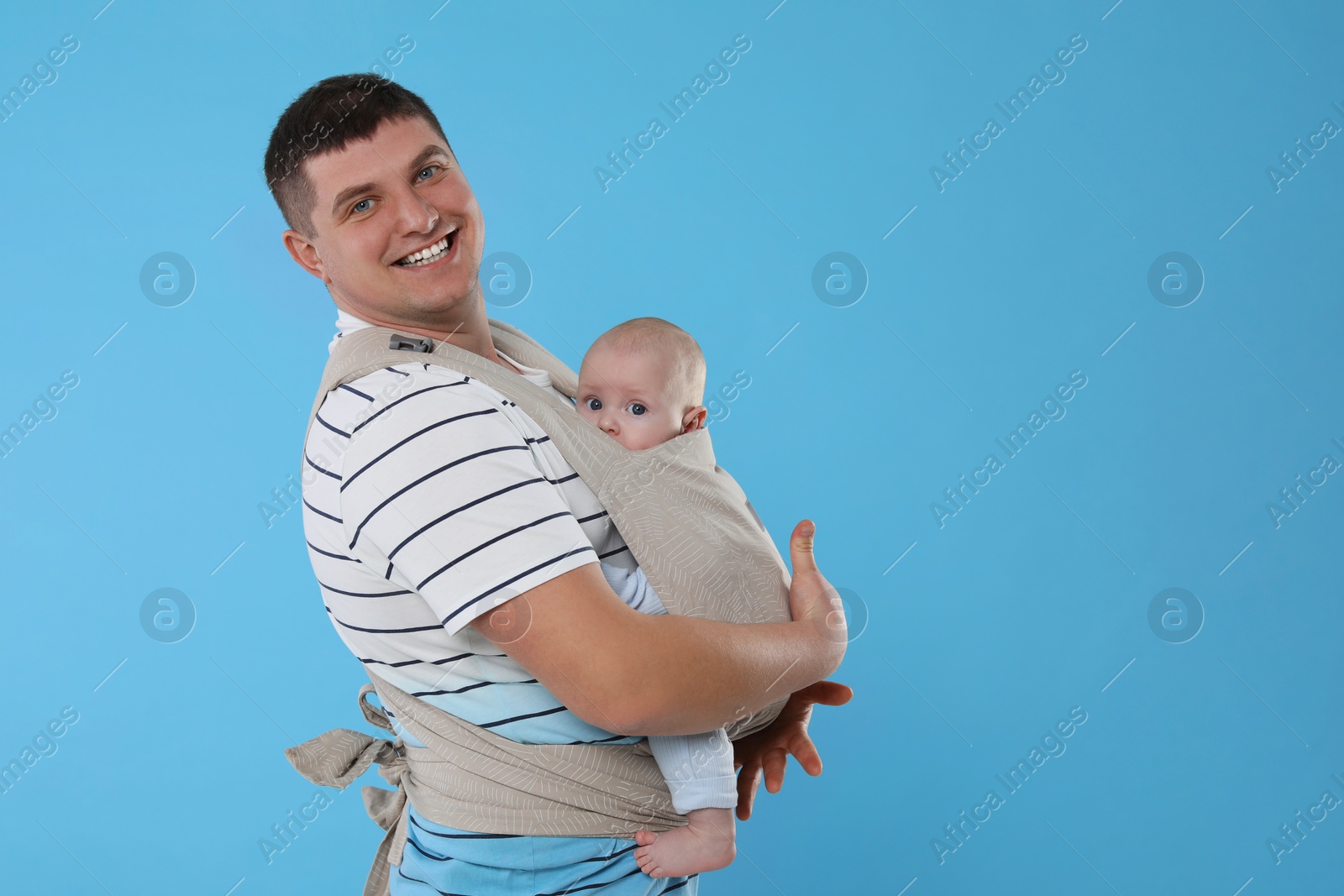 Photo of Father holding his child in sling (baby carrier) on light blue background. Space for text