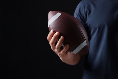 Athletic man with American football ball on black background, closeup. Space for text