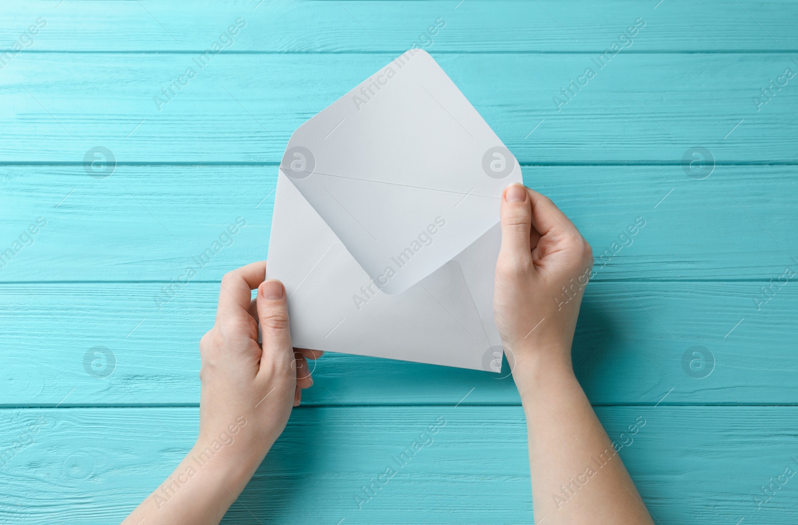 Photo of Woman with white paper envelope at light blue wooden table, top view