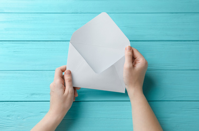 Photo of Woman with white paper envelope at light blue wooden table, top view