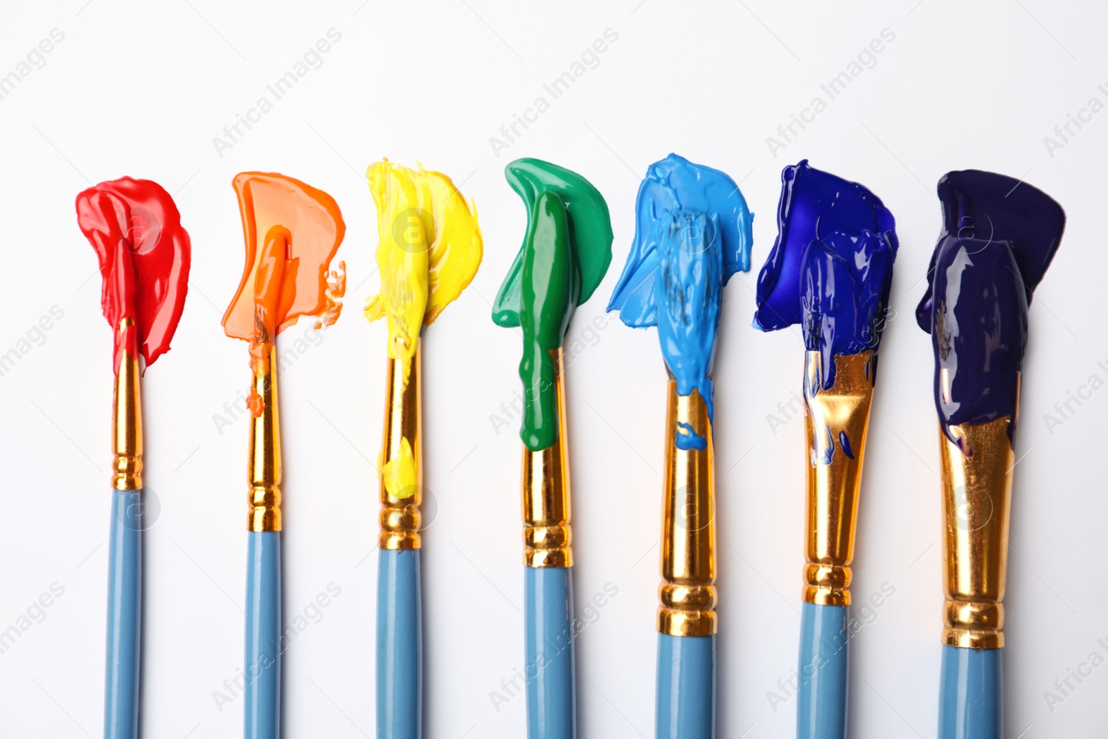 Photo of Set of brushes with different paints on white background, flat lay. Rainbow colors