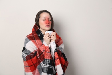 Image of Young woman with blanket sneezing on light background, space for text. Runny nose