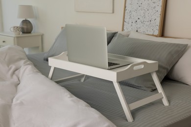 Photo of White tray table with laptop on bed indoors