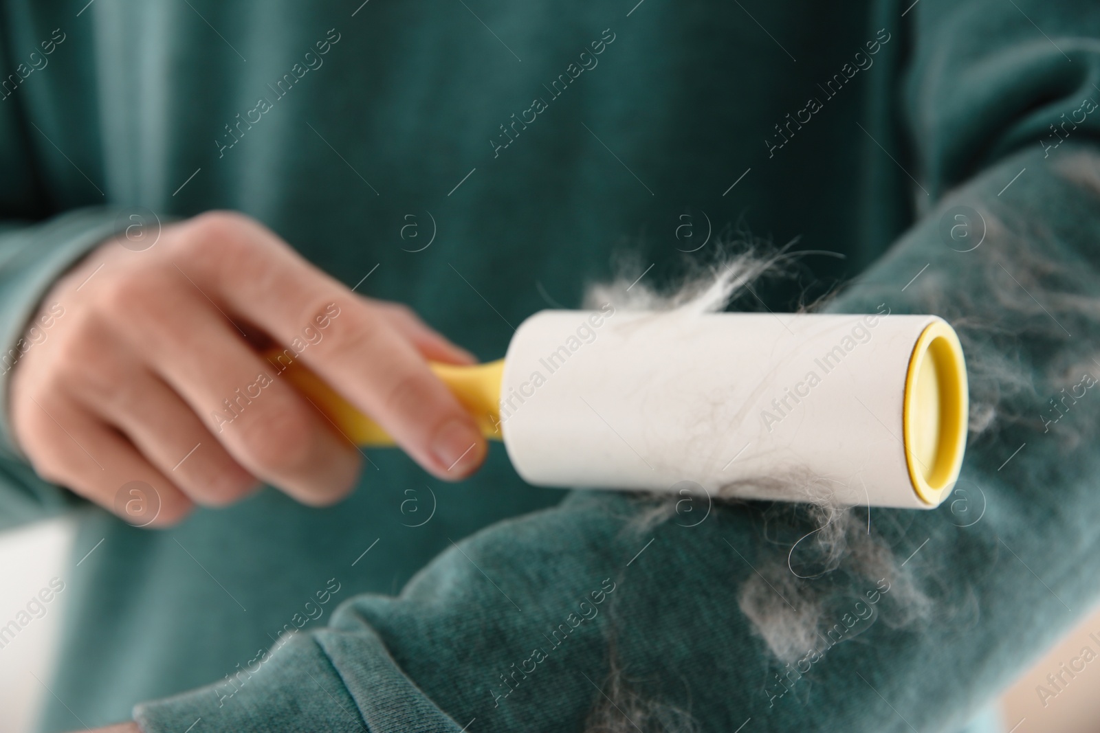 Photo of Man removing hair from green sweatshirt with lint roller on light background, closeup