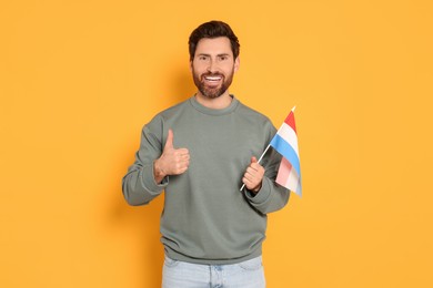 Photo of Man with flag of Netherlands showing thumb up on yellow background