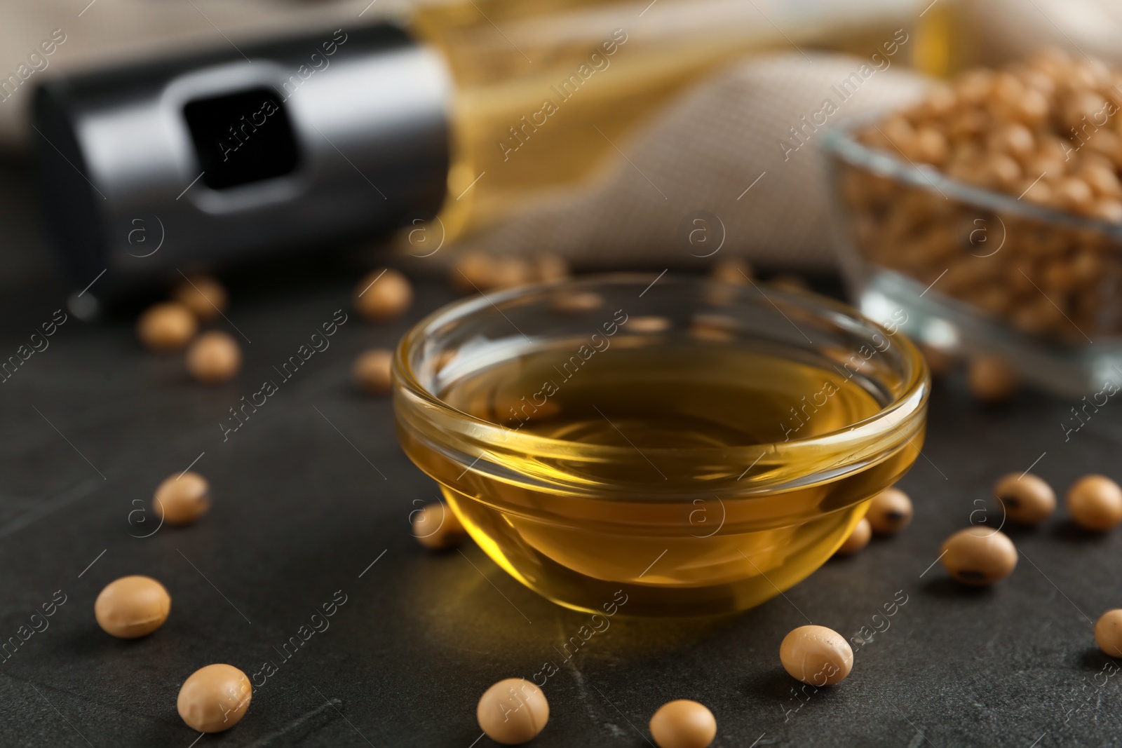 Photo of Soybeans and bowl of oil on grey table, closeup