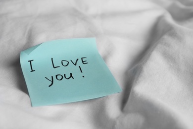 Photo of Sticky note with phrase I love you! on bed, closeup. Space for text