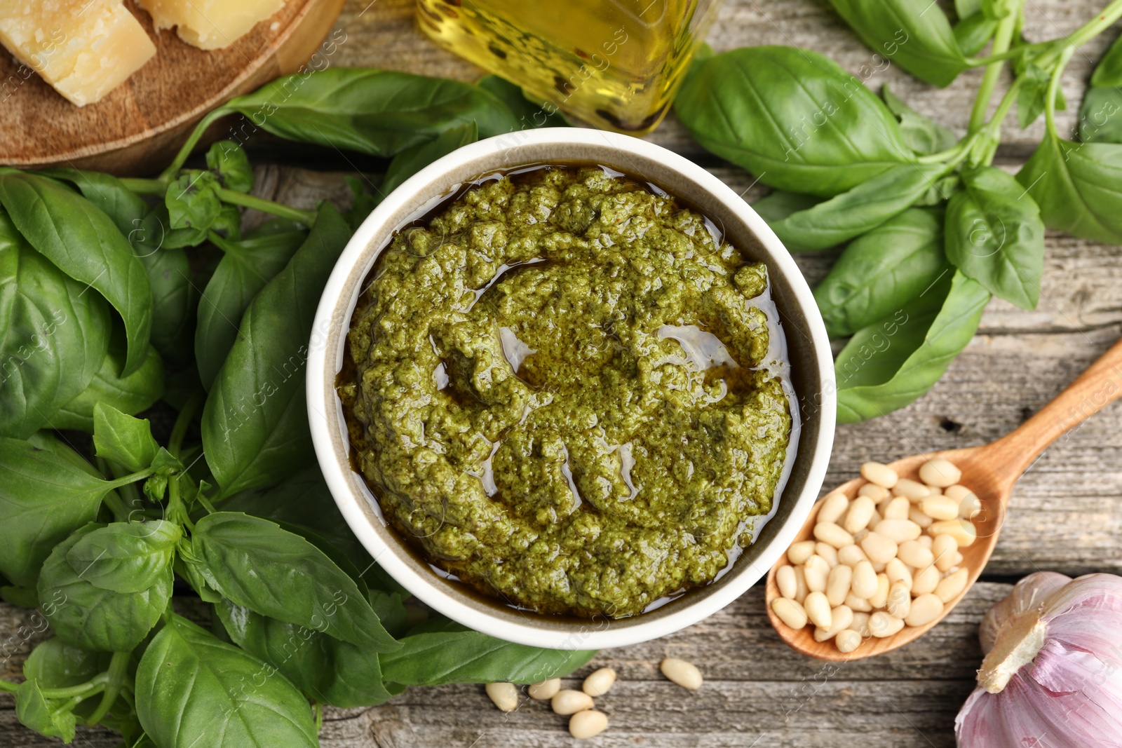 Photo of Tasty pesto sauce in bowl, pine nuts, garlic and basil on wooden table, flat lay