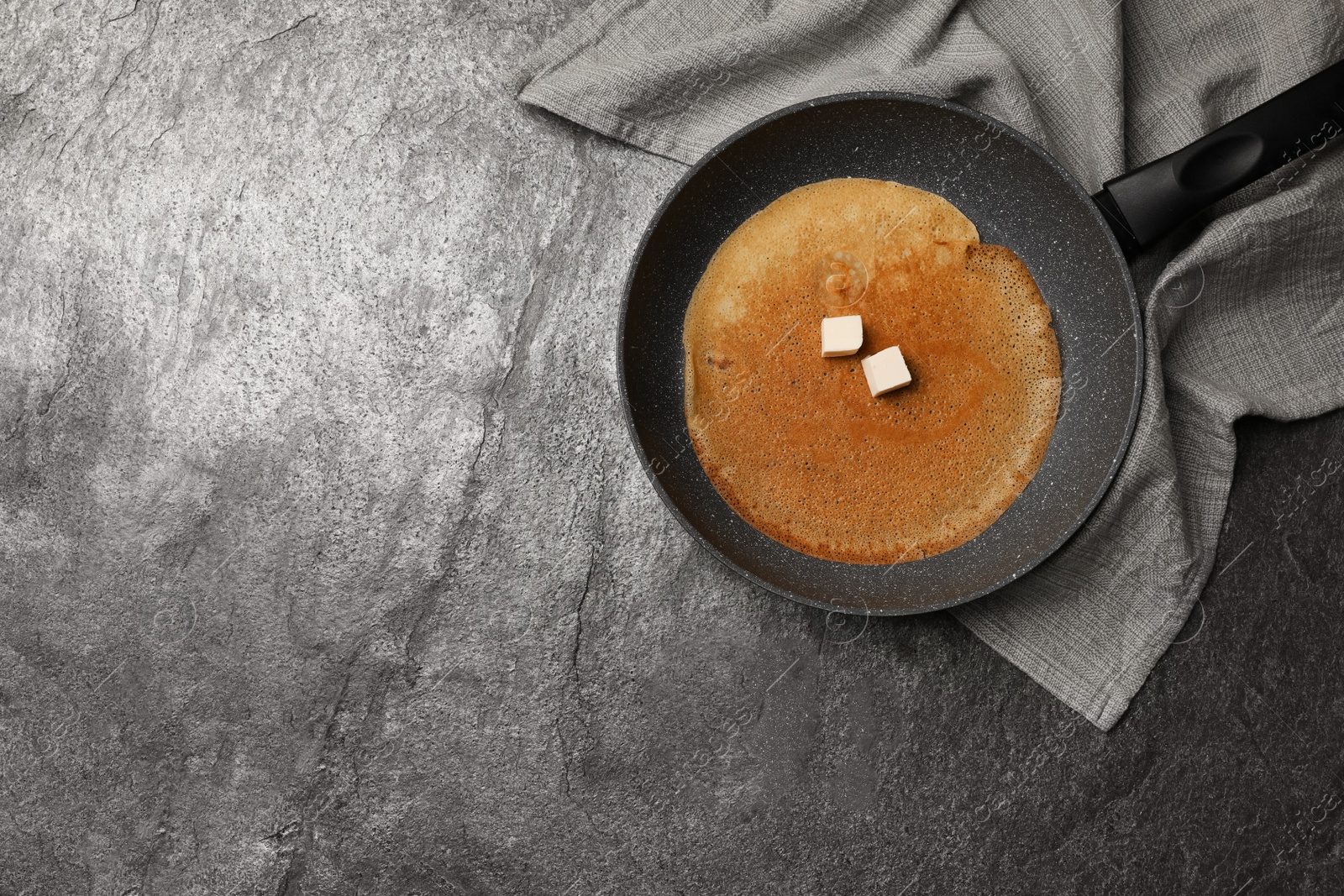 Photo of Frying pan with delicious crepe and napkin on grey table, top view. Space for text