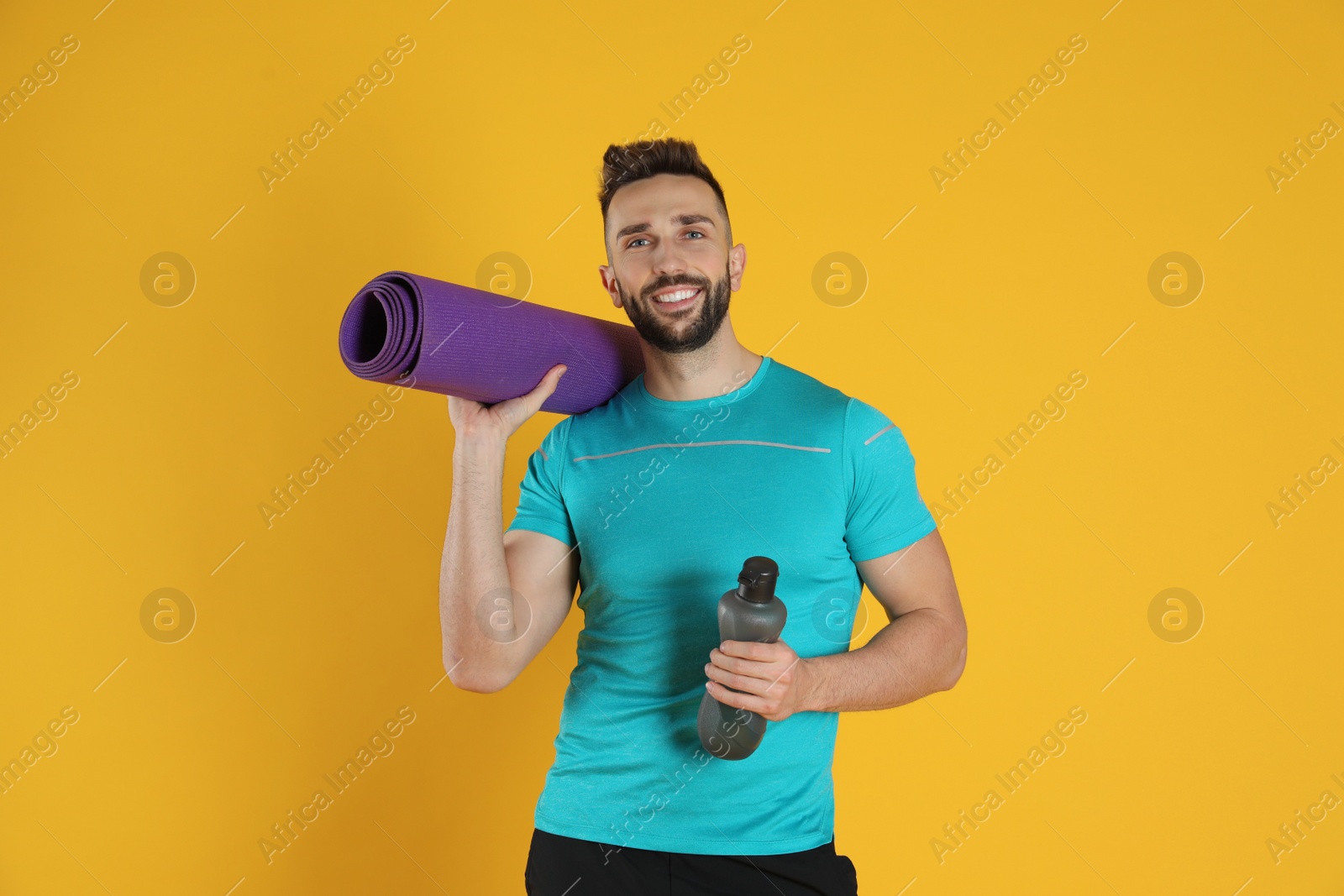 Photo of Handsome man with yoga mat and bottle of water on yellow background