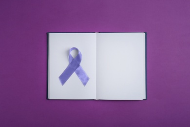 Purple awareness ribbon and open notebook on color background, top view with space for text