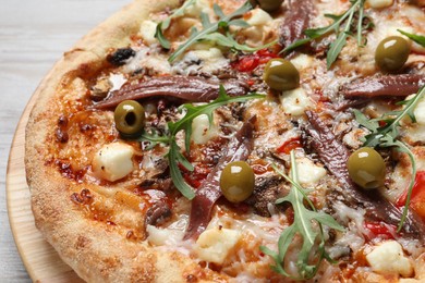 Photo of Tasty pizza with anchovies, arugula and olives on grey wooden table, closeup