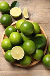 Fresh limes and green leaves on wooden table, flat lay