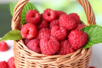 Photo of Tasty ripe raspberries and green leaves in wicker basket, closeup