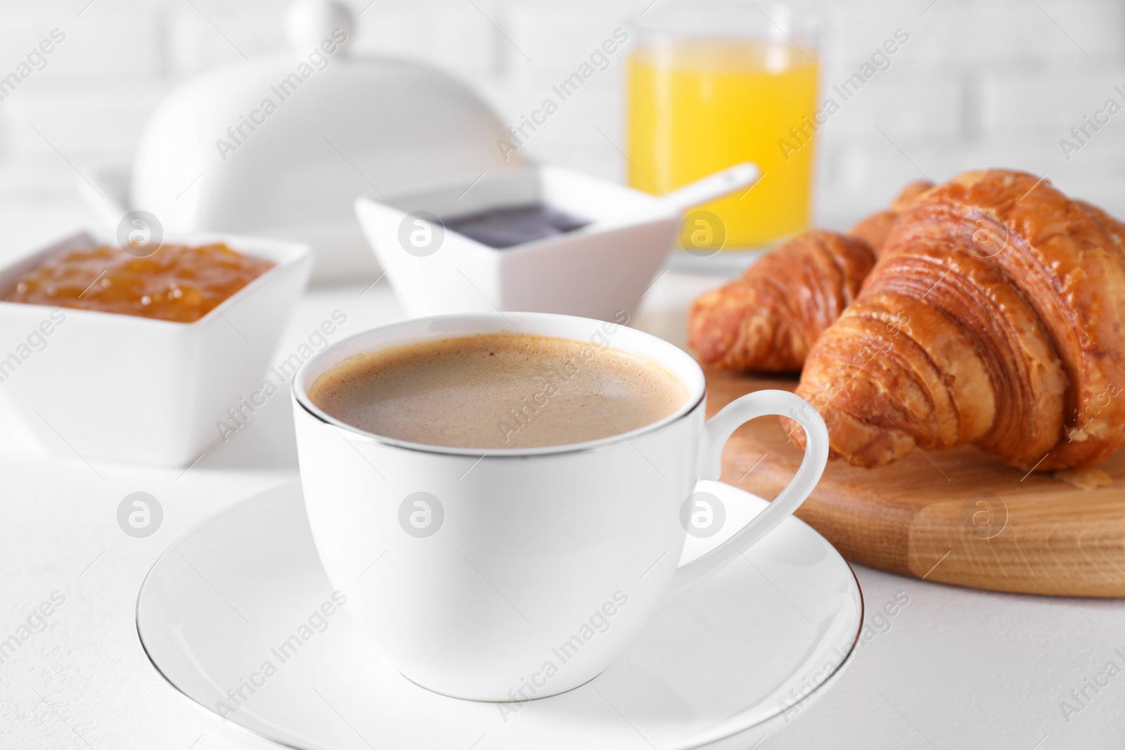 Photo of Fresh croissants, jams and coffee on white table, closeup. Tasty breakfast