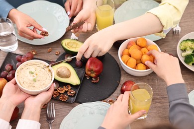 Friends eating vegetarian food at wooden table indoors, closeup