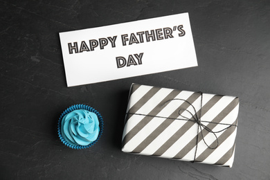 Photo of Cupcake, gift box and card with phrase HAPPY FATHER'S DAY on black table, flat lay