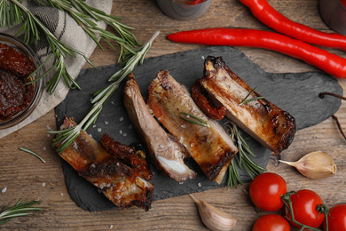 Tasty grilled ribs with rosemary on wooden table, flat lay