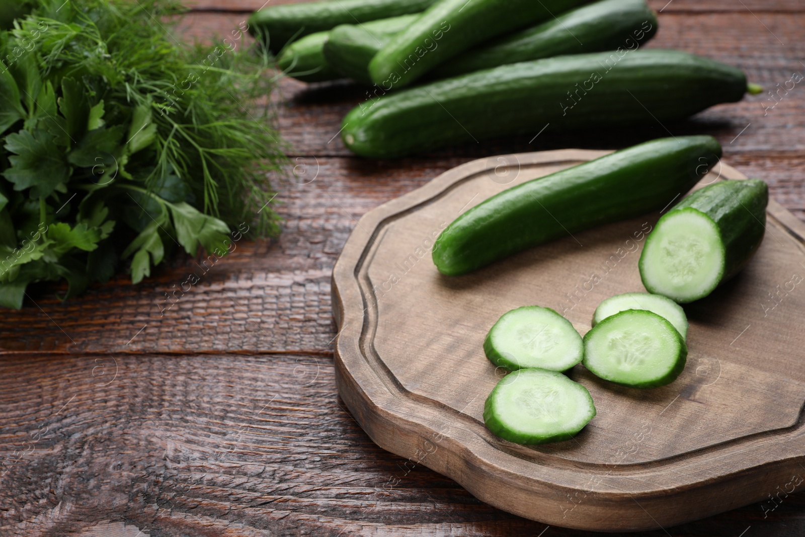 Photo of Fresh ripe cucumbers, parsley and dill on wooden table
