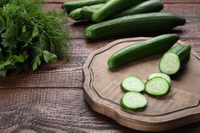 Photo of Fresh ripe cucumbers, parsley and dill on wooden table