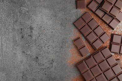 Delicious dark chocolate and cocoa powder on grey table, flat lay. Space for text