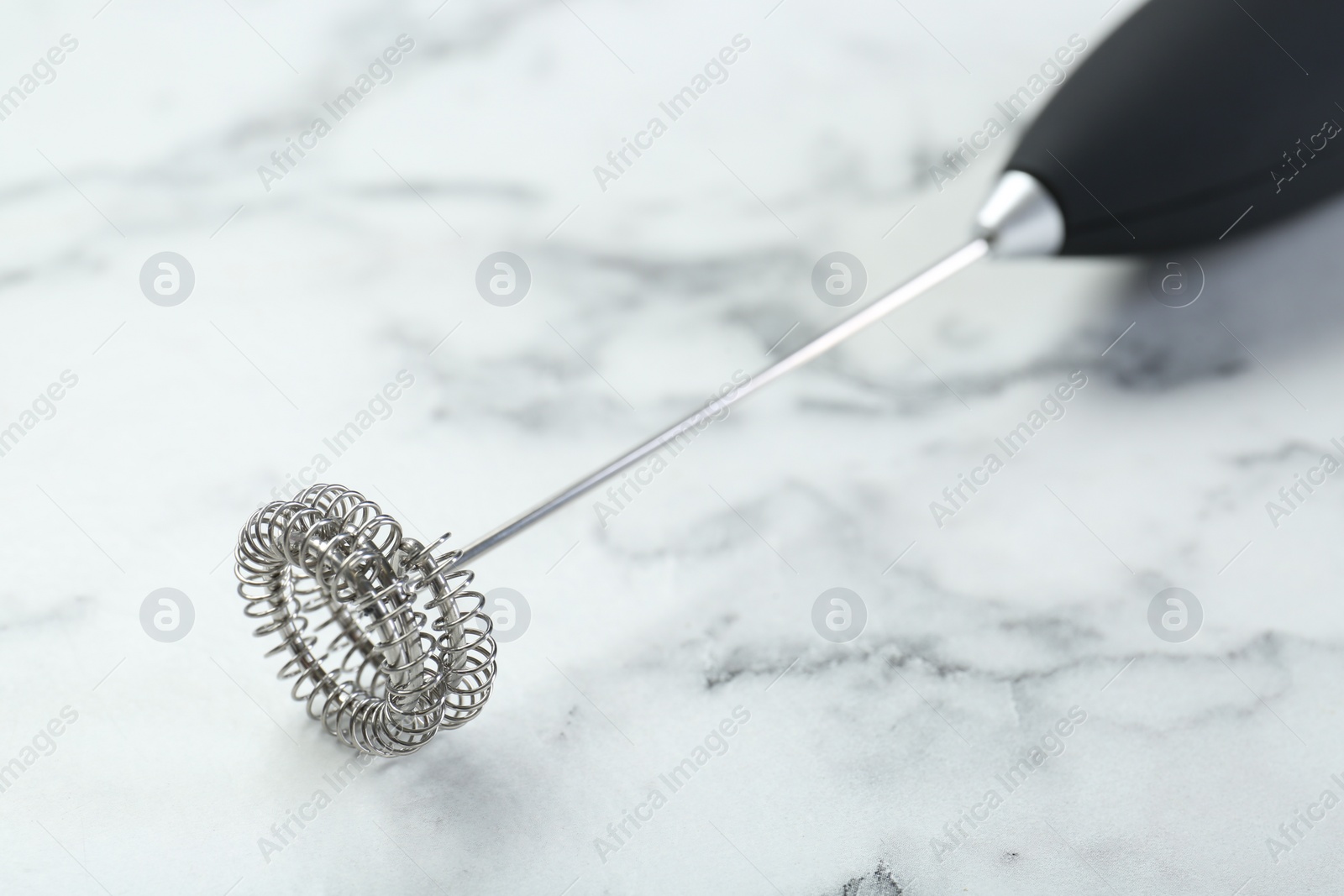 Photo of Black milk frother wand on white marble table, closeup