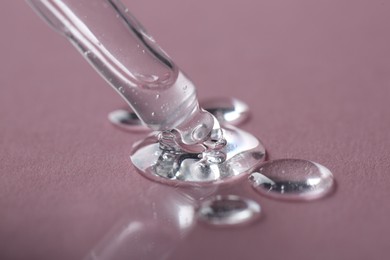 Photo of Dripping cosmetic serum from pipette onto pink background, macro view