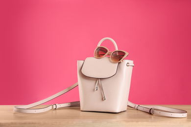 Stylish woman's bag and sunglasses on wooden table