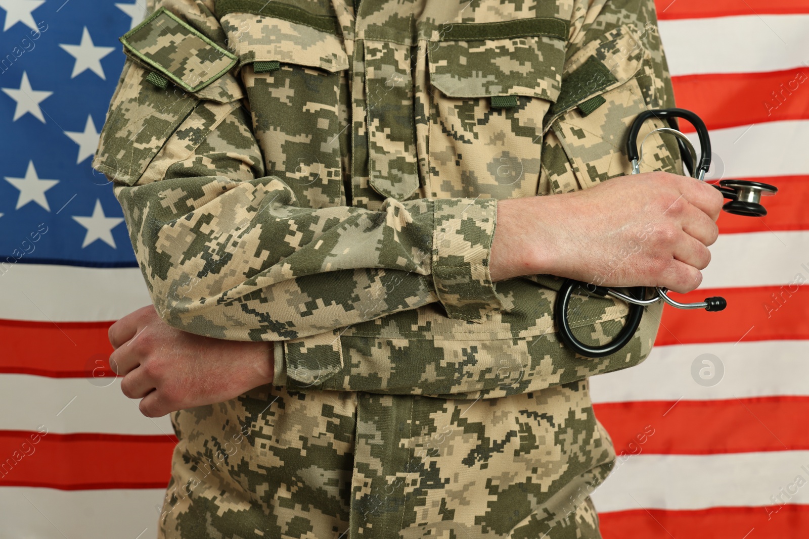 Photo of Man in military uniform with crossed arms and stethoscope against USA flag, closeup. Health care concept