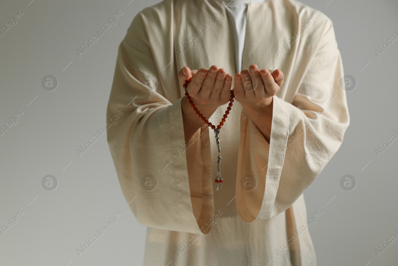 Photo of Muslim man with misbaha praying on light grey background, closeup. Space for text