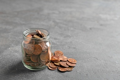 Glass jar and coins on grey table. Space for text