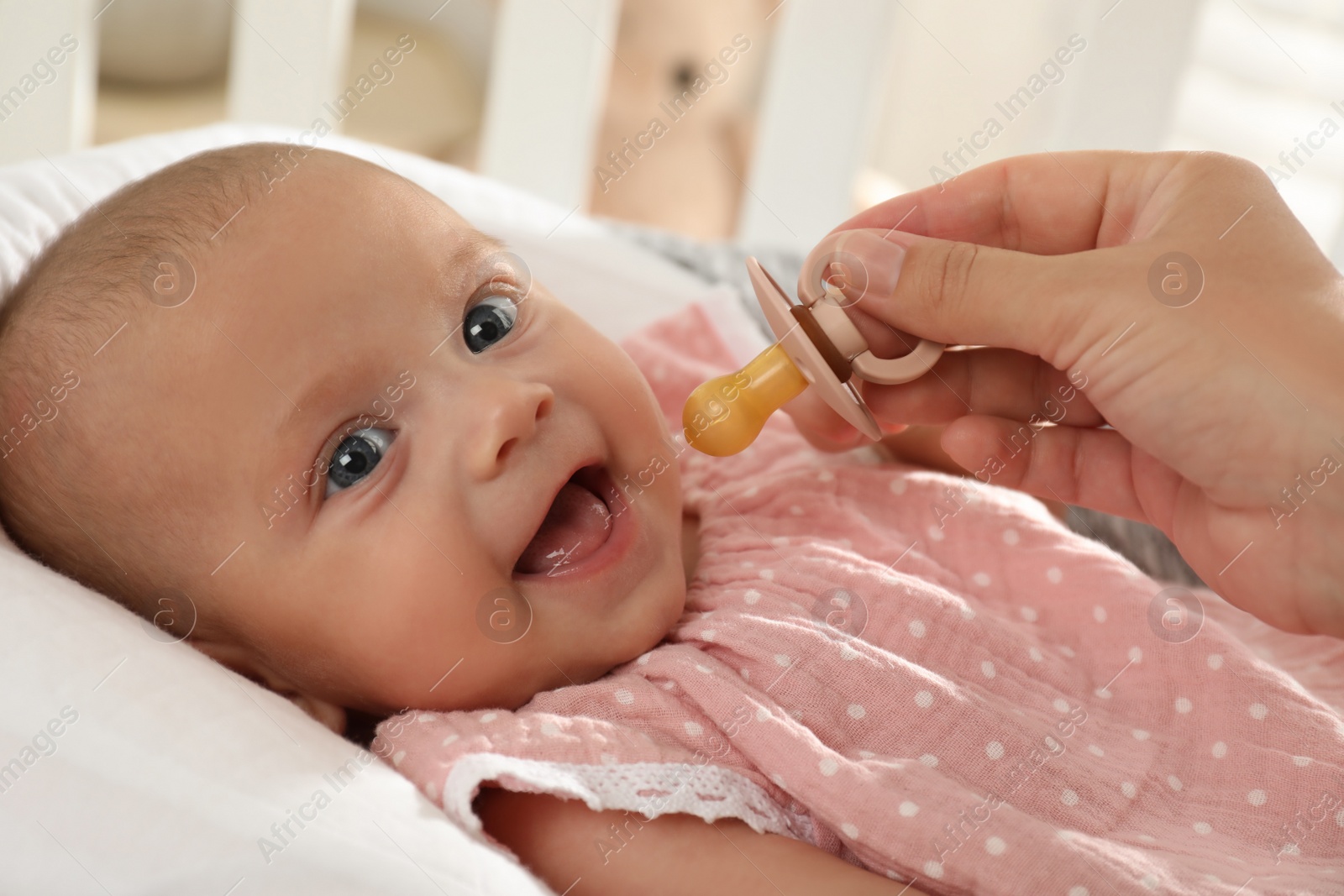 Photo of Mother giving pacifier to cute little baby in soft crib, closeup