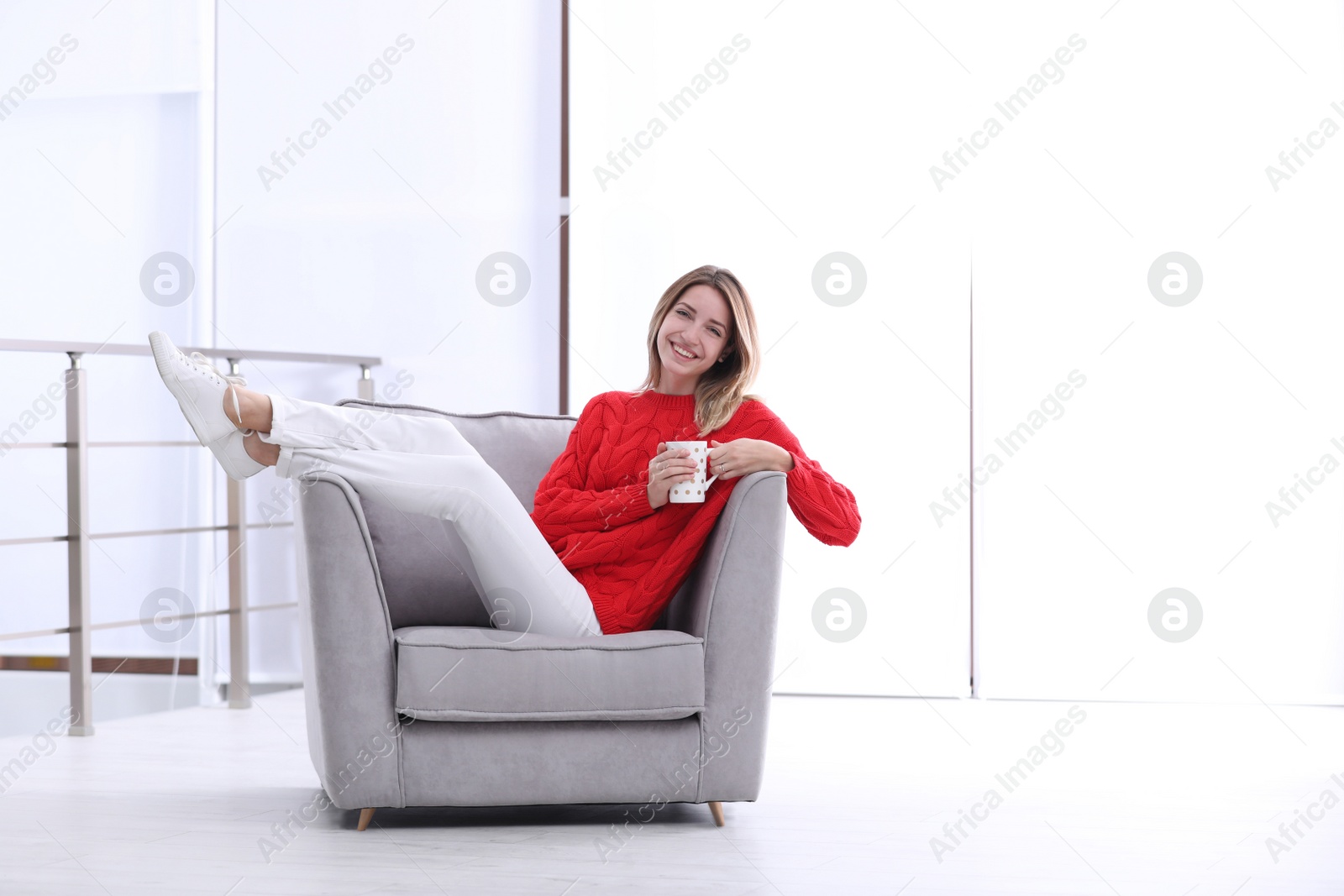 Photo of Attractive young woman with cup of tea in armchair indoors. Space for text
