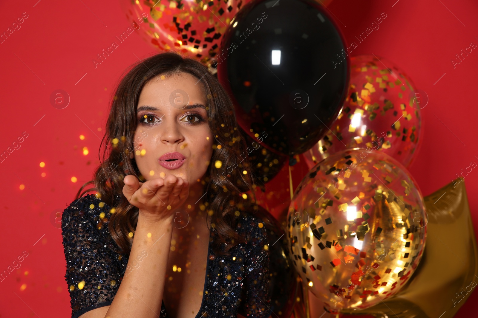 Photo of Happy woman with air balloons blowing glitter on red background. Christmas party