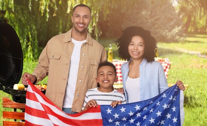 Image of 4th of July - Independence day of America. Happy family with national flag of United States having picnic in park