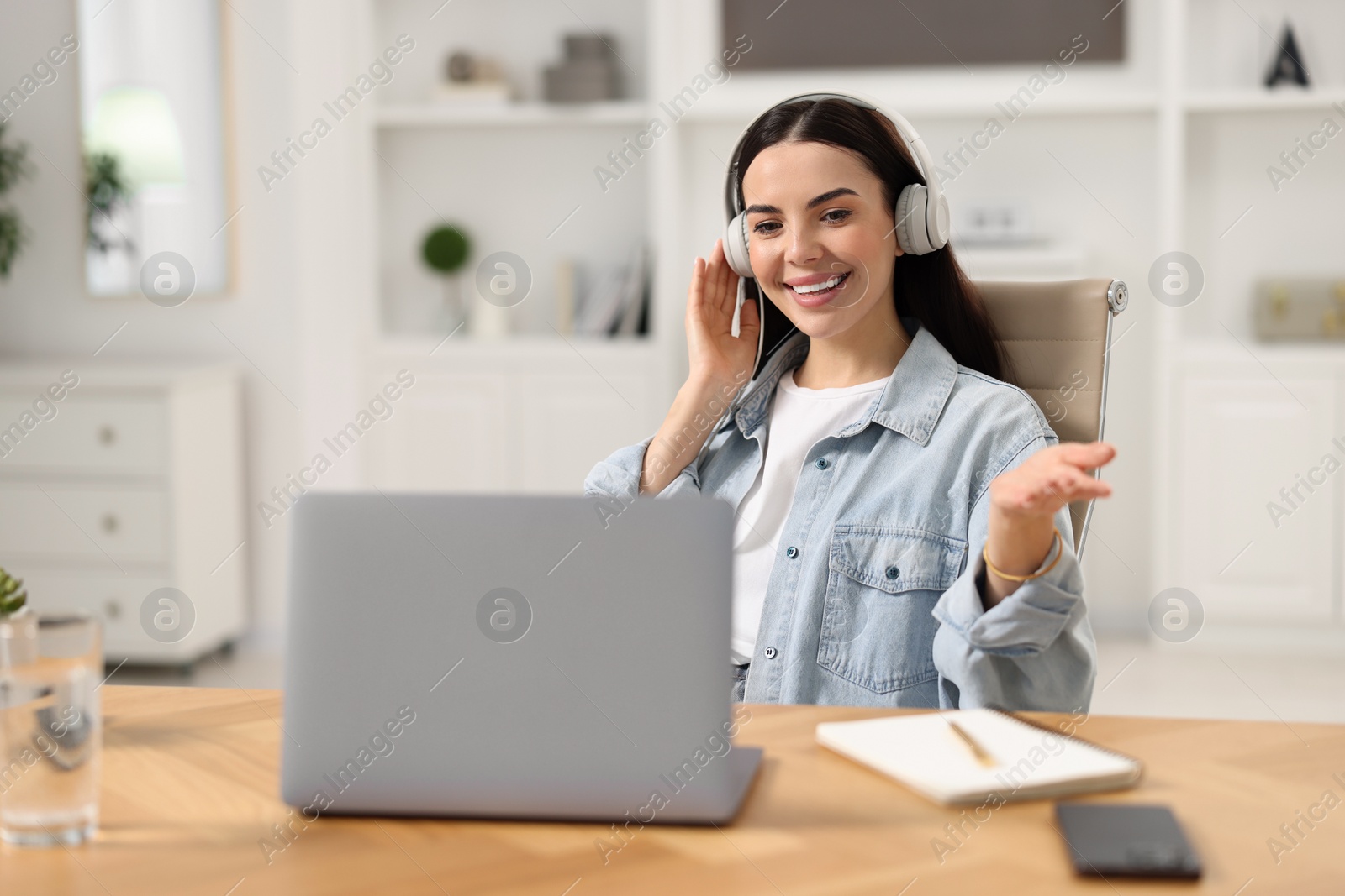 Photo of Young woman in headphones using video chat during webinar at table in room