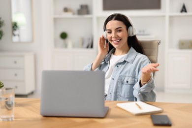 Young woman in headphones using video chat during webinar at table in room