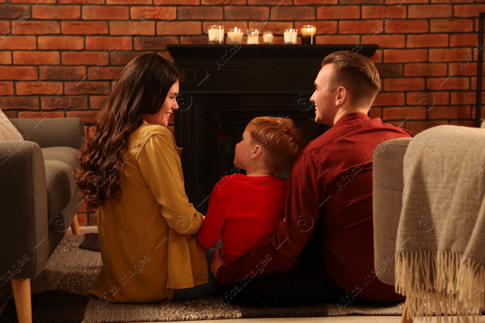 Photo of Happy family spending time together on floor near fireplace at home, back view